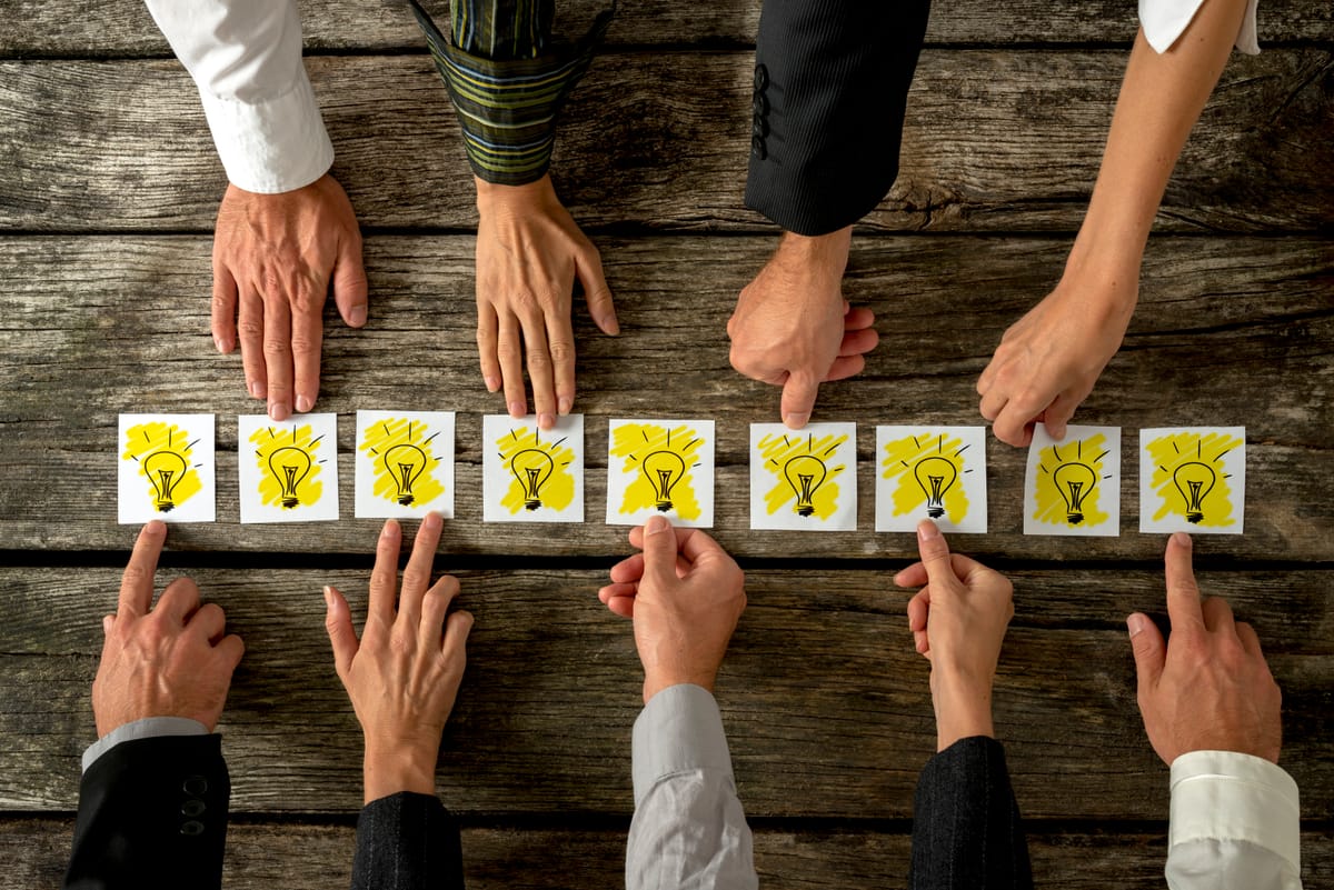 Hands pointing to light bulbs on a table, representing mental models, decision-making, and different perspectives.