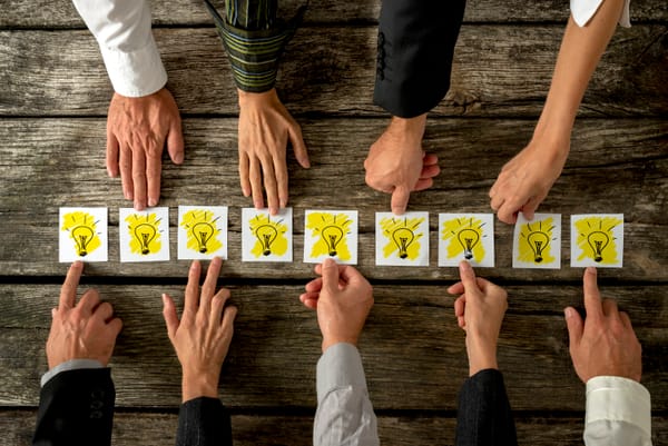 Hands pointing to light bulbs on a table, representing mental models, decision-making, and different perspectives.